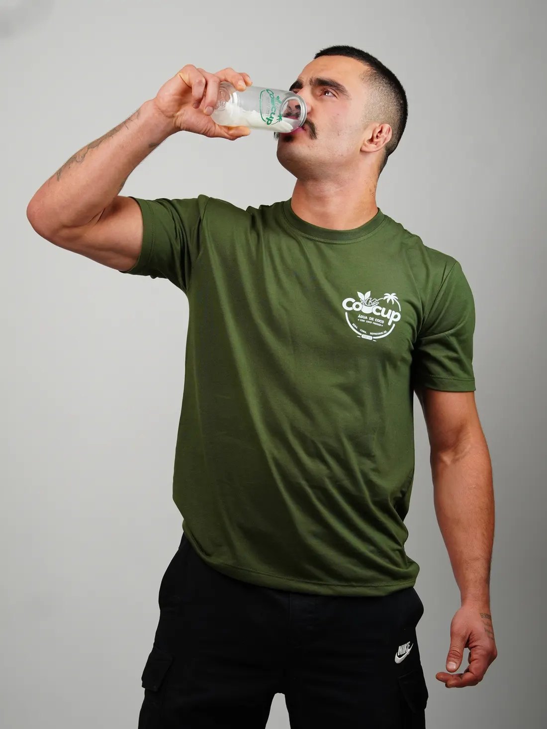 Homem de camiseta verde com o logo da Cocup bebendo de um copo de Cocup