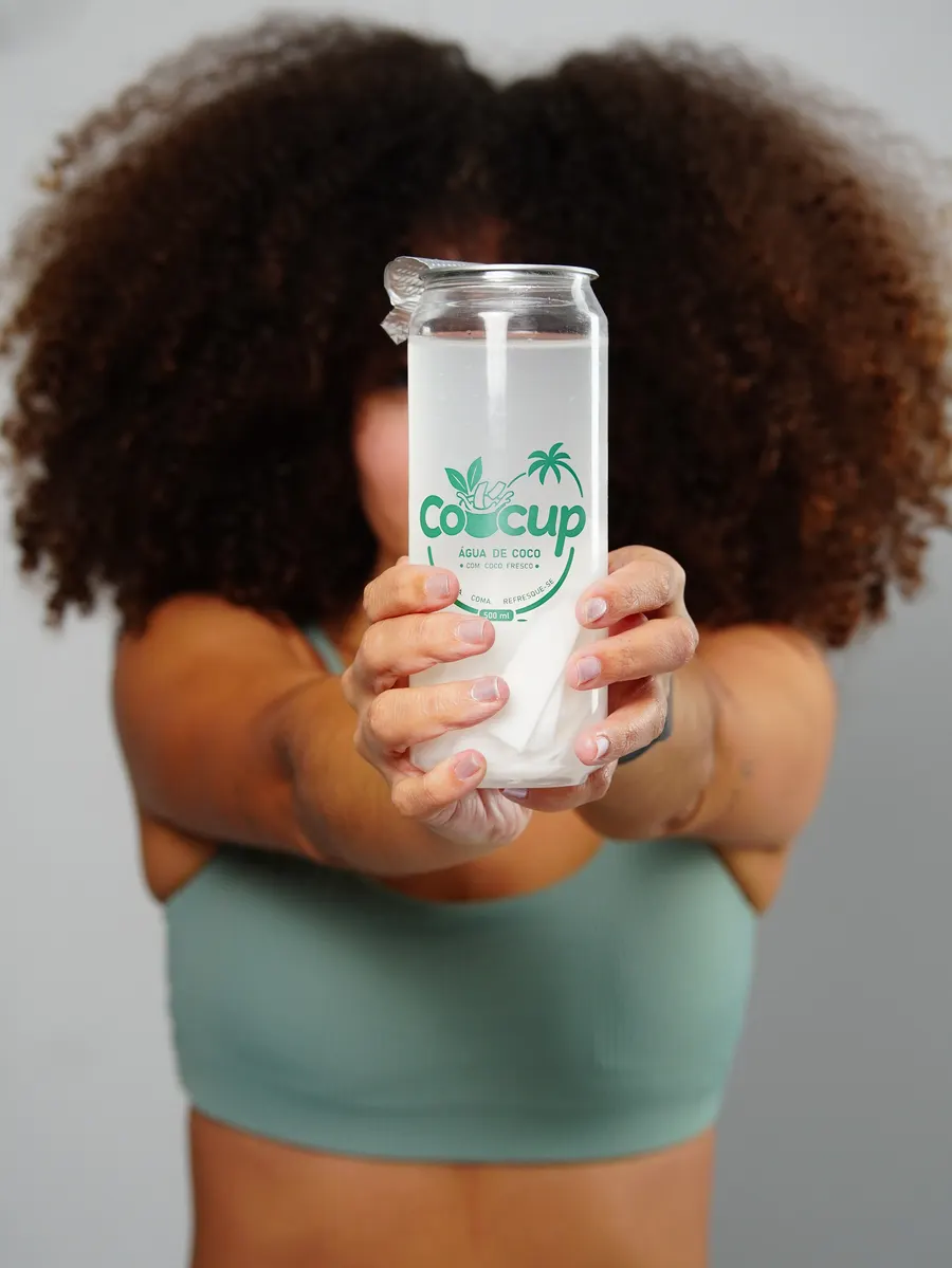 Copo de Cocup estendido em direção à câmera, com água de coco e pedaços de coco