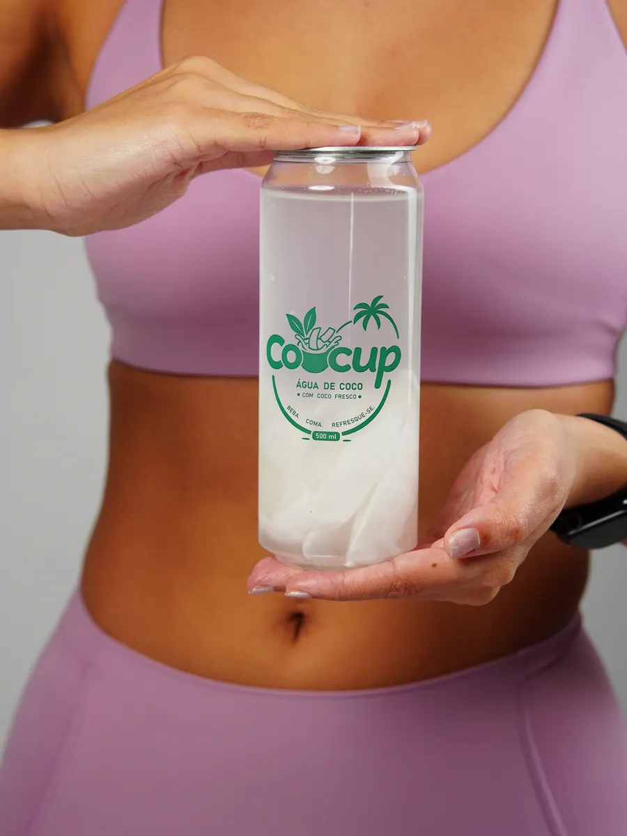 Mãos apoiando um copo de Cocup com água de coco e pedaços de coco