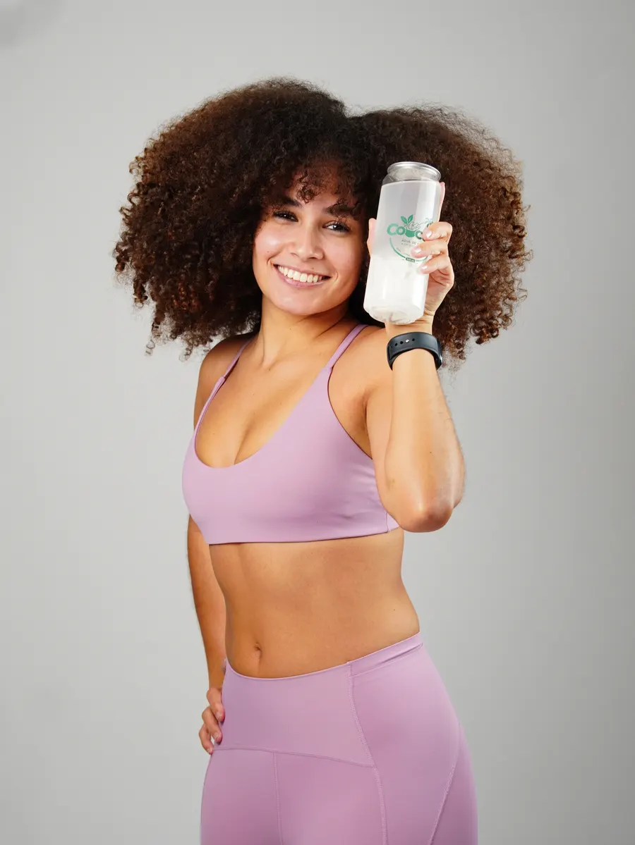 Mulher sorrindo, de top e legging lilás, segurando um copo de Cocup junto ao rosto